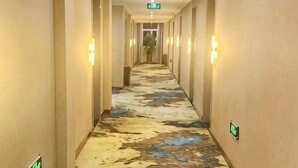 A hotel hallway with a patterned floor, light fixtures on the walls, and an exit sign. - Shangpin Business Hotel (Guangde)