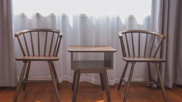 A room with two wooden chairs and a small table, a window with sheer curtains, and a wooden floor.