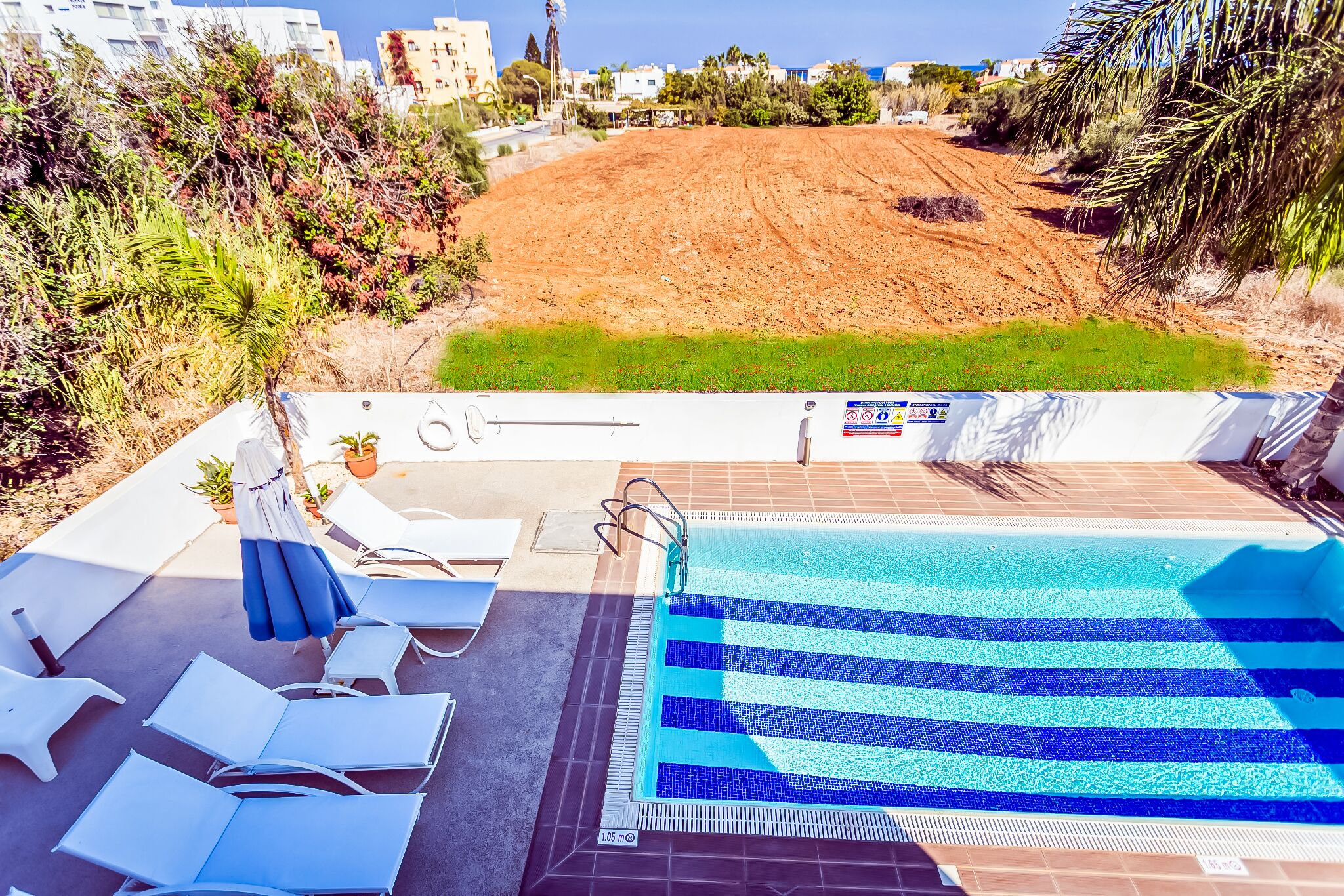 A swimming pool with a tiled deck, lounge chairs, and a safety sign.