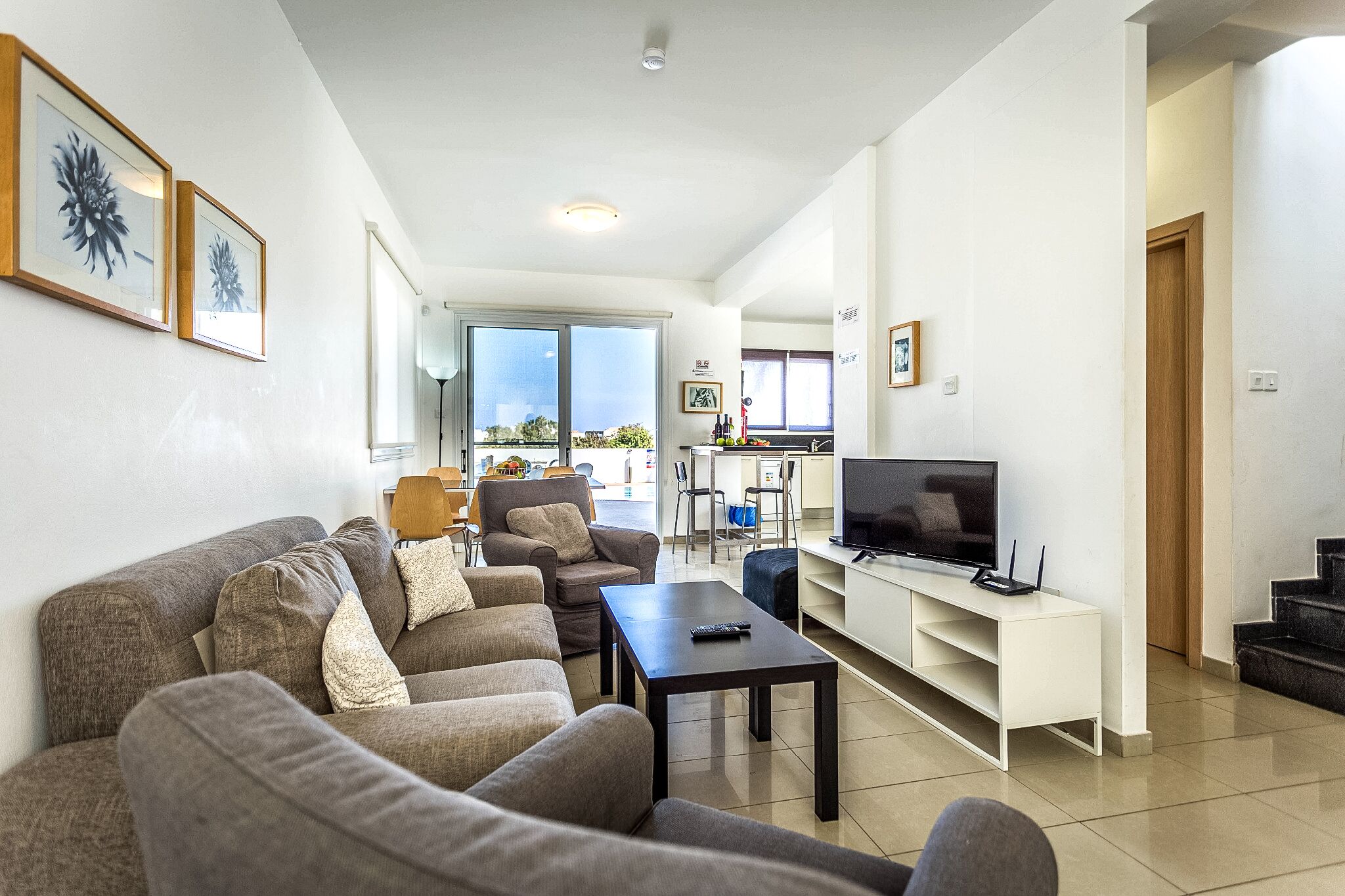 Ein modernes Wohnzimmer mit einer Sofagarnitur, einem Couchtisch, einem Fernseher und einem Essbereich mit Stühlen.