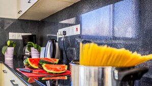 A kitchen counter with a pot of spaghetti, a cutting board with watermelon slices, and a knife.