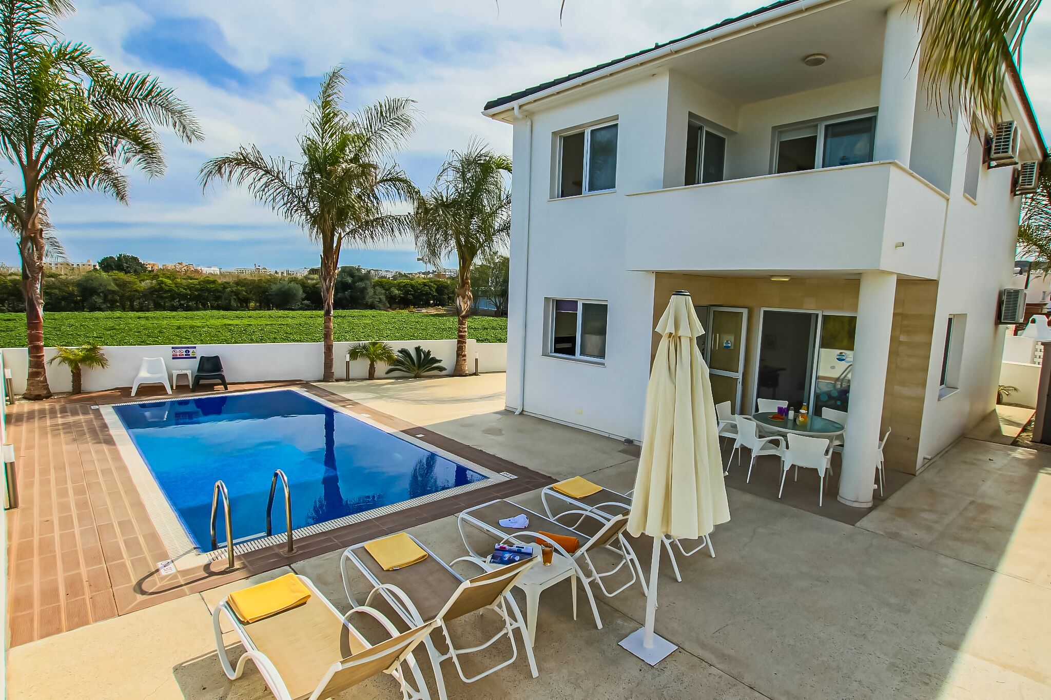 Una casa moderna de dos pisos con piscina, mobiliario exterior y palmeras.