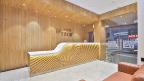 Zona de recepción de hotel con un mostrador de madera y una pared de vidrio.
