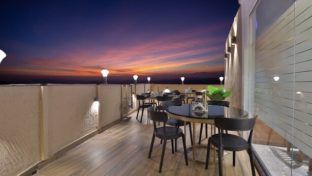 Una terraza en la azotea con suelo de madera, mesas redondas y sillas negras, que ofrece vistas al atardecer.