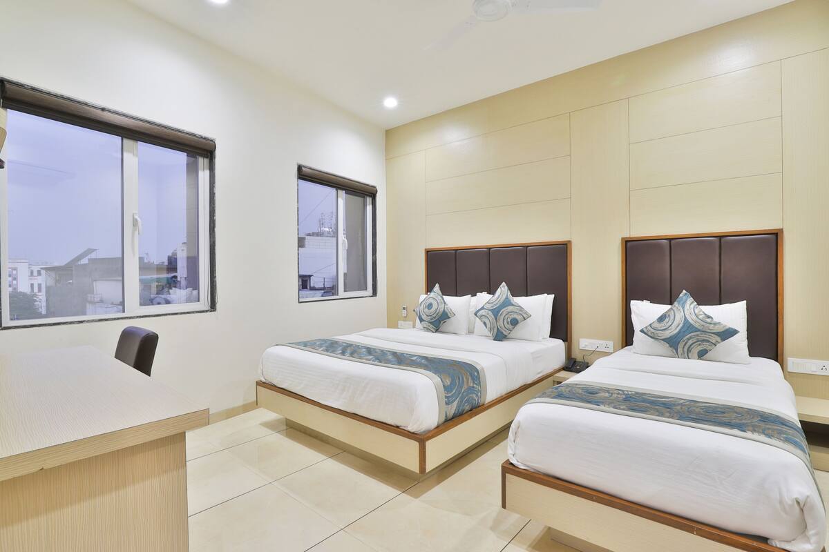 A hotel room with two beds, a desk, and a window.