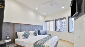 Un dormitorio moderno con una cama grande, una mesita de noche, un televisor montado en la pared y ventanas amplias con vistas a la ciudad.
