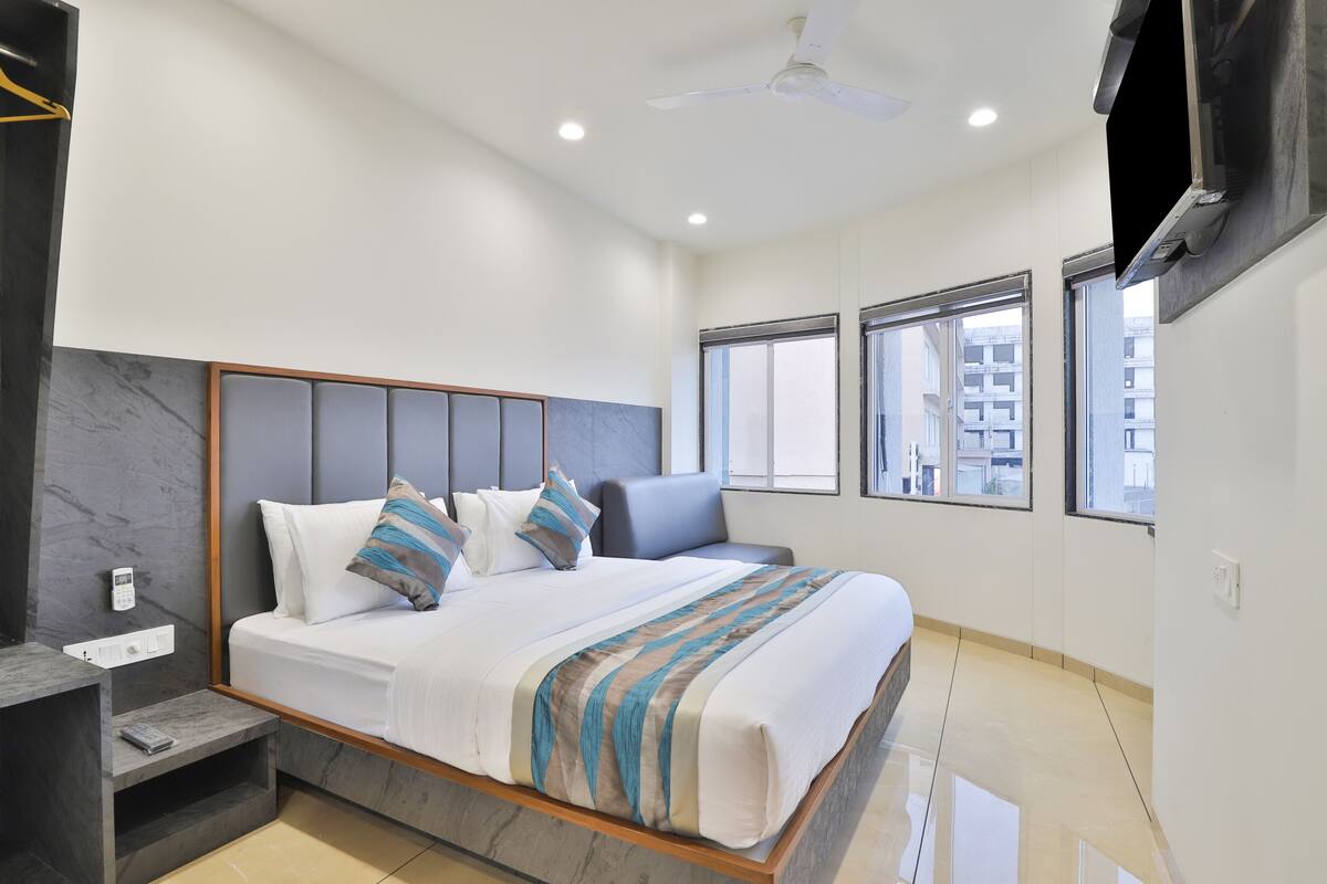 A modern bedroom with a large bed, a nightstand, a TV mounted on the wall, and large windows with a city view.