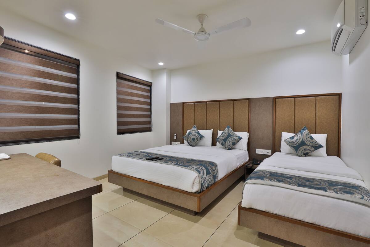 A hotel room with two beds, a desk, and a ceiling fan.