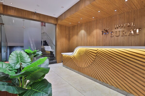 A hotel reception area with a wooden reception desk and a staircase in the background. - HOTEL SURAT (Surat)