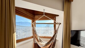 A room with a hammock chair, a wooden floor, a TV, and a window with a view of mountains. - Cozy appartment with great mountan view (Bruneck)