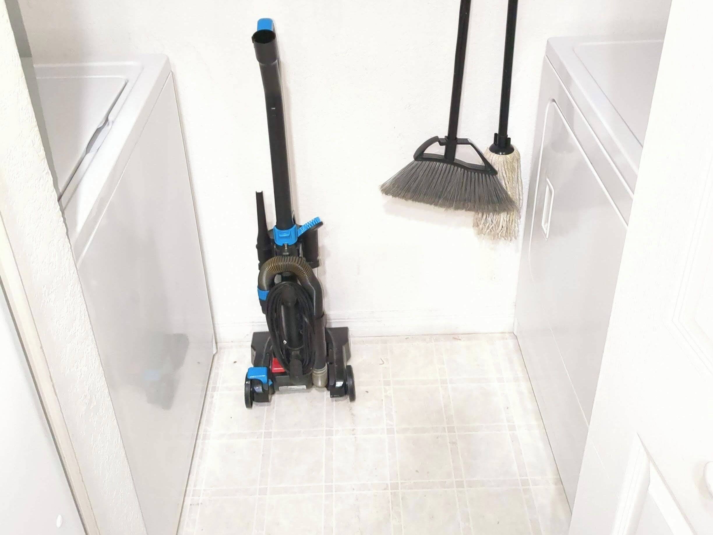 A corner of a room with a vacuum cleaner and a broom leaning against the wall.