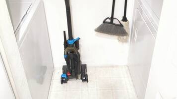 A corner of a room with a vacuum cleaner and a broom leaning against the wall.