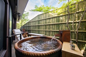 Un jacuzzi con una mesa y sillas de madera, una cerca de bambú y vista a árboles.