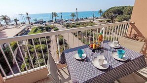 A balcony with a table set for two, overlooking a coastal road with parked cars and palm trees.