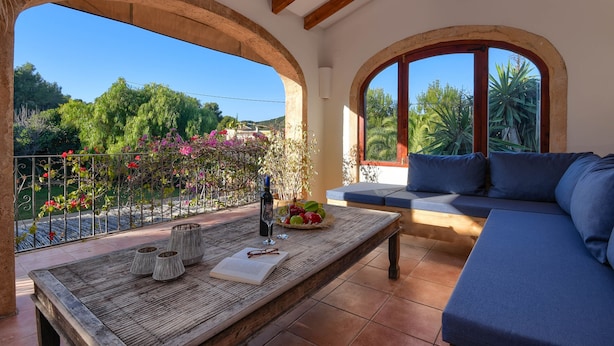 Un balcón con mesa de madera, un sofá y vistas a zonas verdes y árboles.