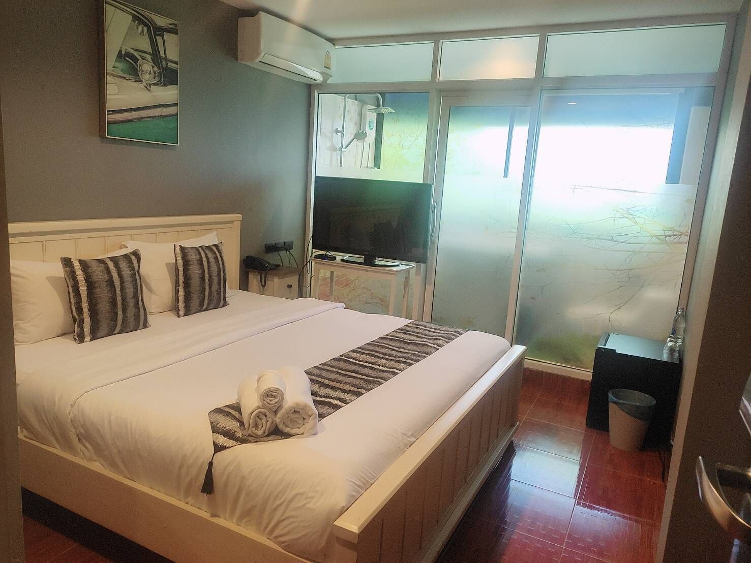 Habitación de hotel con una cama grande, televisión, escritorio y puerta corrediza de vidrio a un balcón.