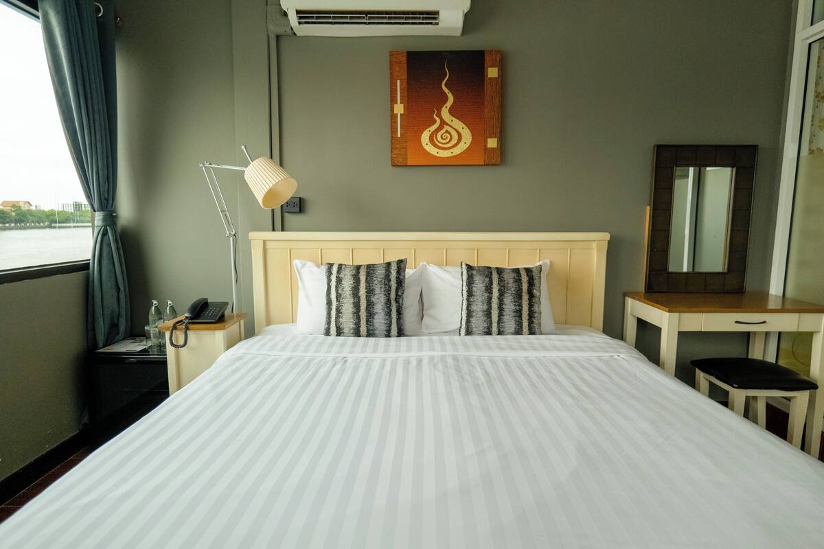A hotel room with a large bed, a bedside table with a lamp, a desk, a mirror, and a painting on the wall.