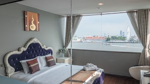 A hotel room with a large bed, a desk, and a view of a cityscape and water. - Anandpura Riverside Hotel (Bangkok)