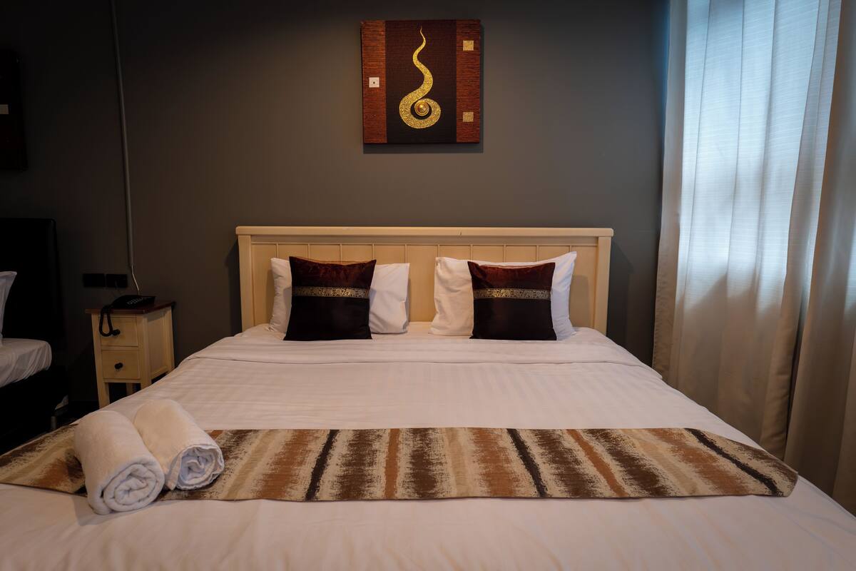 A hotel room with a bed, two pillows, a headboard, a wall art piece, a nightstand, and a rolled towel.