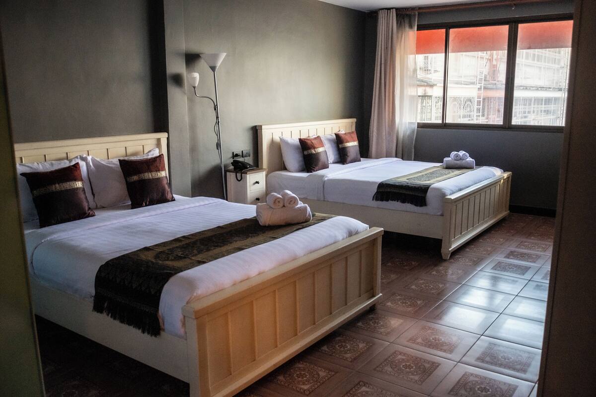 Hotellihuone, jossa on kaksi sänkyä, yöpöytä lampun kanssa ja ikkuna, jossa on verhot.
