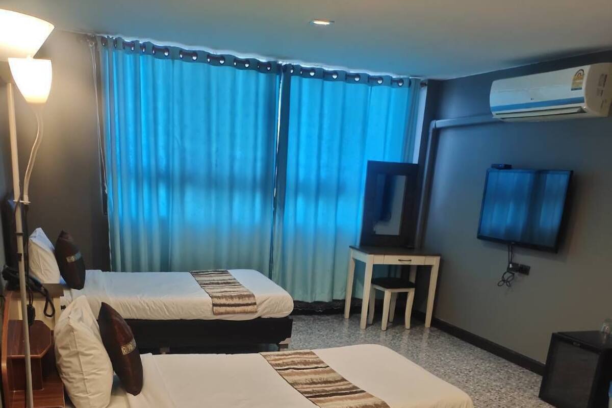 Hotellihuone, jossa on kaksi sänkyä, työpöytä, televisio ja ilmastointilaite.