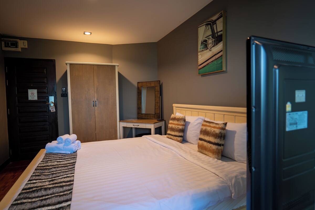 A hotel room with a bed, a desk, a wardrobe, and a mirror.