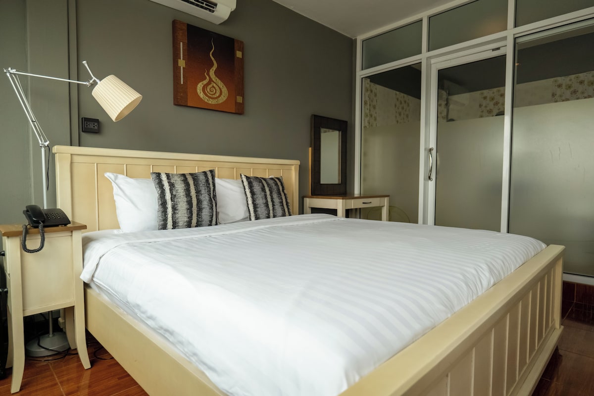 Una cama con ropa de cama blanca, una lámpara de noche, un teléfono y un cuadro en la pared.