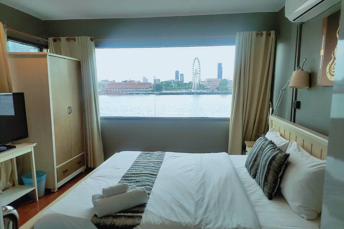 Hotellihuone, jossa on sänky, televisio, työpöytä sekä näkymä kaupunkimaisemaan ja vesistöön.