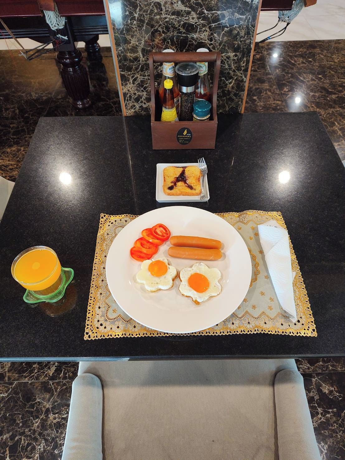 A breakfast table with a plate of eggs, tomatoes, and sausages, a glass of orange juice, and condiments.