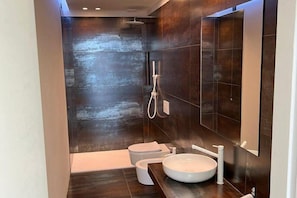 A modern bathroom with dark tiles, a white sink, and a shower. - Villa della Marca: A spacious villa situated a few minutes from the town center, with Free WI-FI. (Assisi)