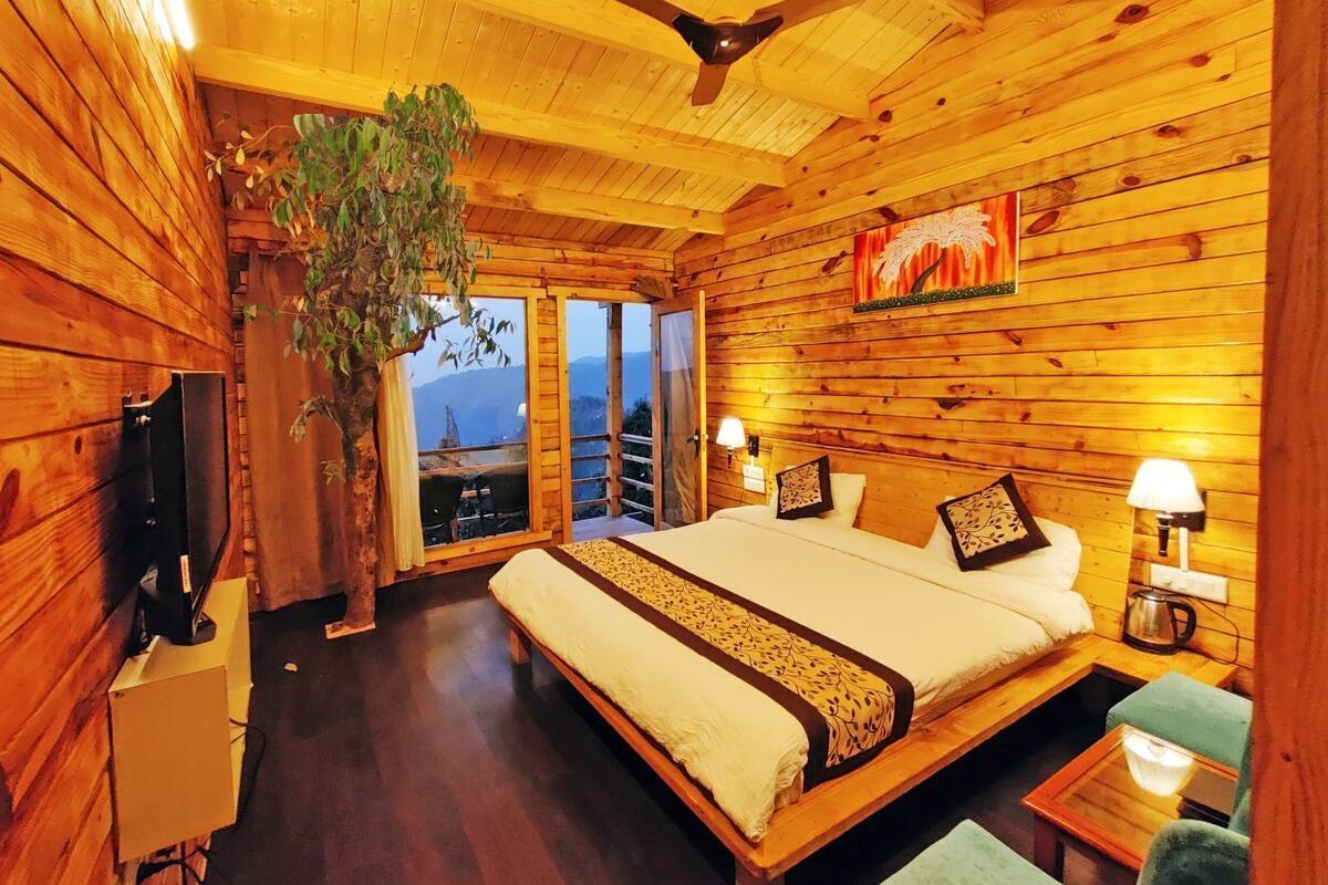 Quarto de cabana de madeira com cama, luminárias de cabeceira, ventilador de teto e uma janela grande.