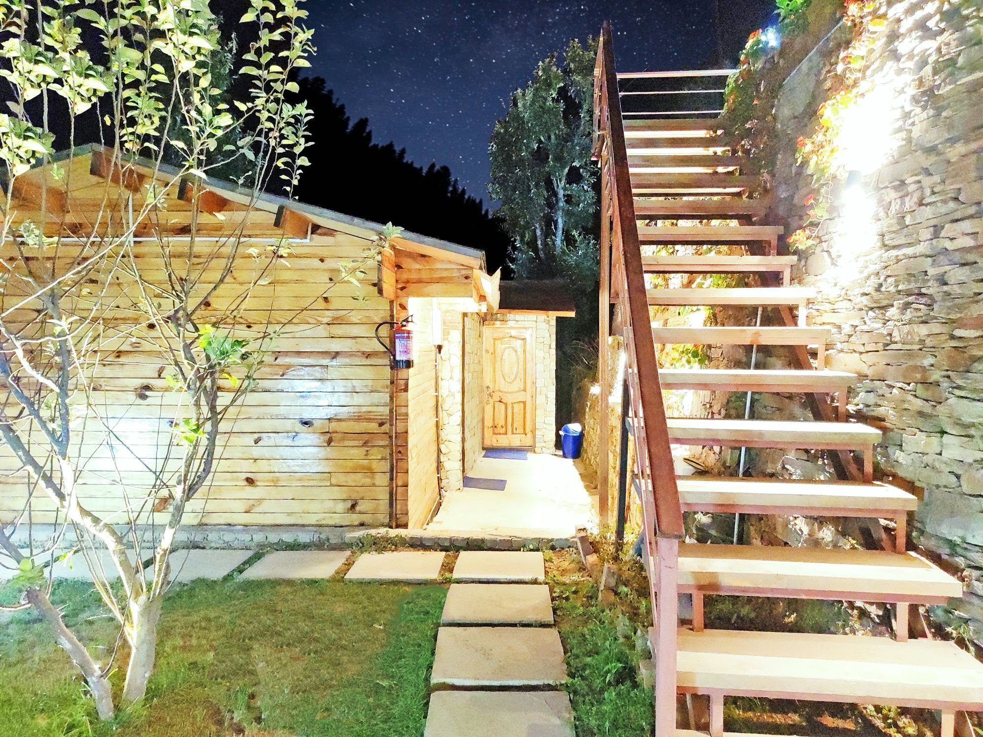 A wooden cabin with a stone wall and a wooden staircase leading to a door.