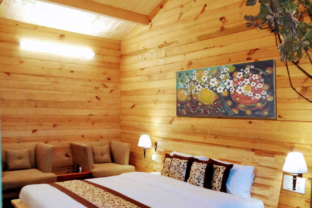 Quarto de cabana de madeira com cama, duas mesinhas de cabeceira, um sofá e um quadro na parede.