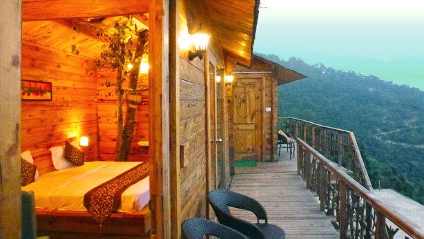 A wooden cabin with a balcony overlooking a mountainous landscape. - Treehouse Resort (Dhari)