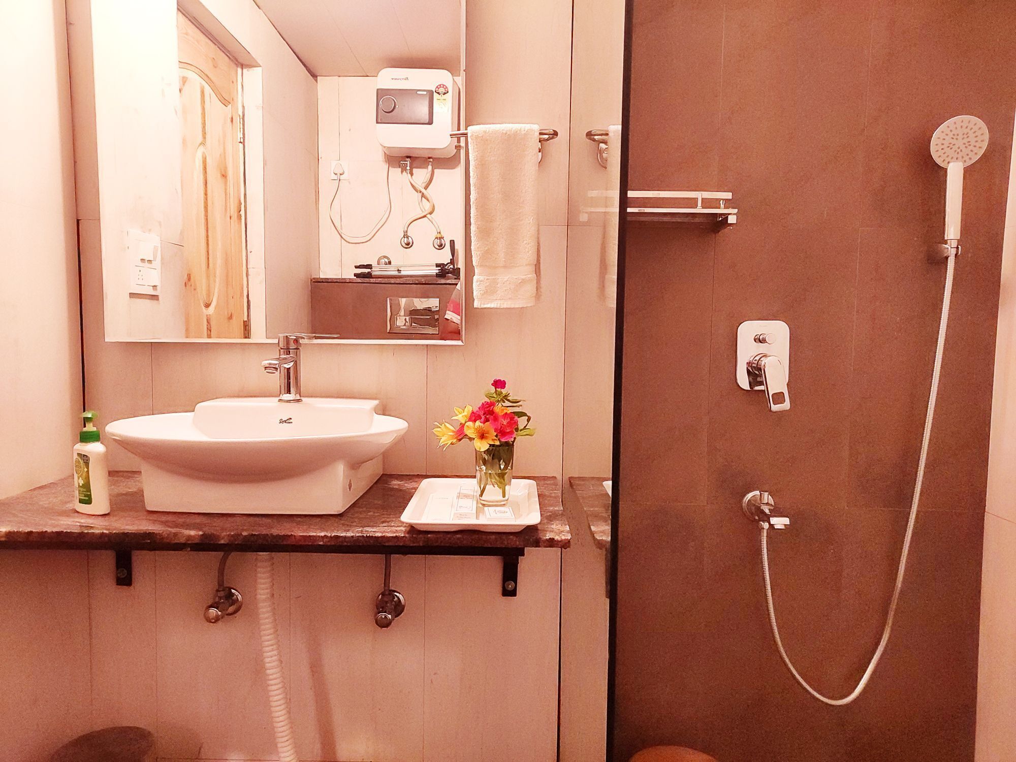 A bathroom with a sink, mirror, towel rack, shower, and a small vase with flowers.