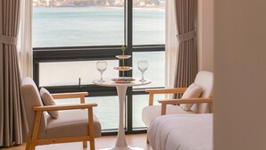Una habitación con vista al mar, que incluye dos sillas, una mesita con un vaso de agua y un plato de comida.