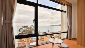 Habitación con un ventanal grande que ofrece vistas al mar y edificios. Hay una mesa redonda con una silla y una alfombra pequeña y circular.