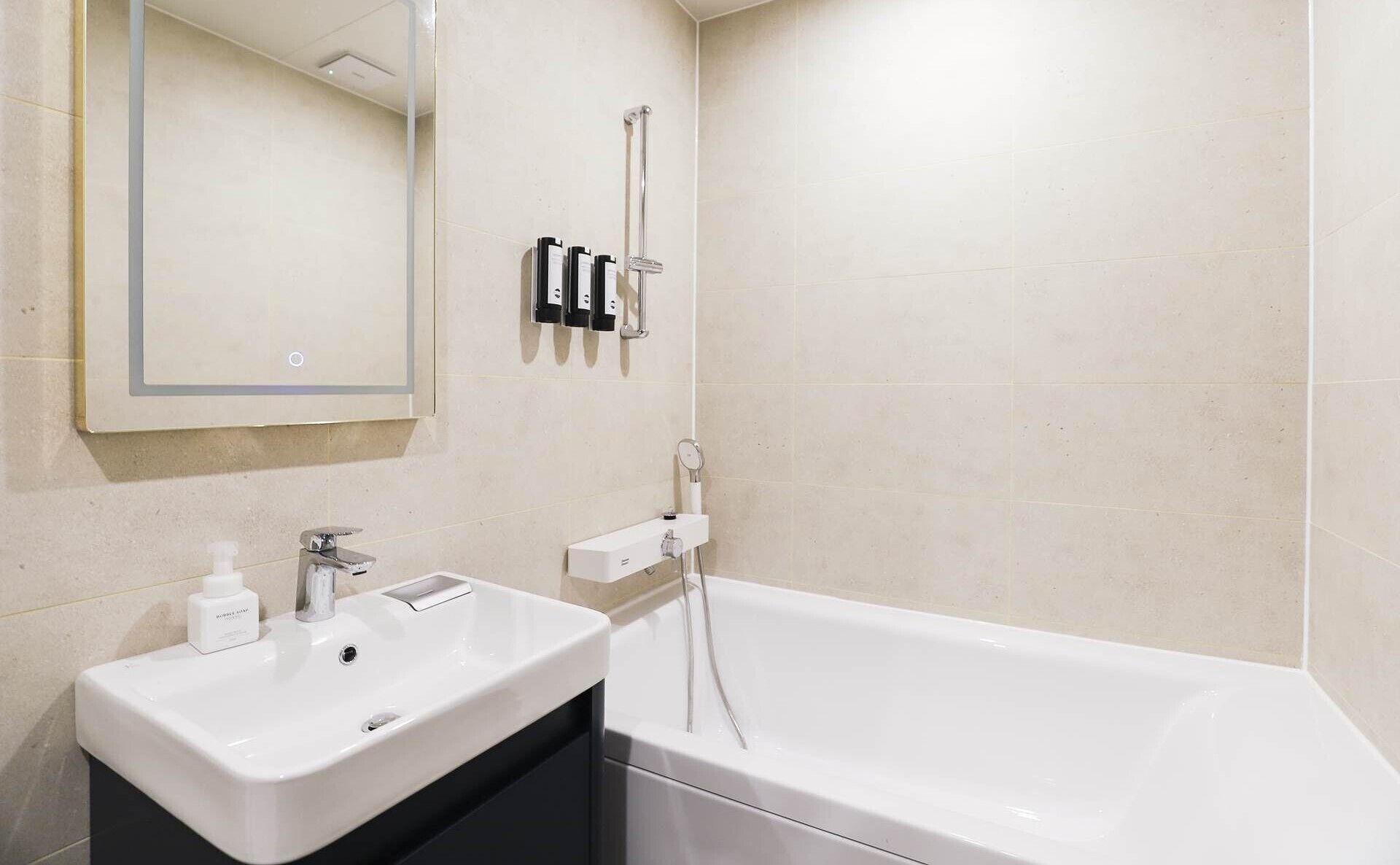 Een moderne badkamer met een wit wastafelmeubel, een spiegel, een handdouche en een bad.