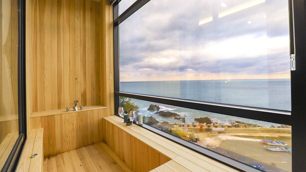 Una habitación de madera con un amplio ventanal con vistas a la costa.