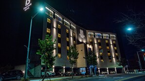 Un hotel moderno con varios pisos, ventanas iluminadas y un estacionamiento con varios automóviles.