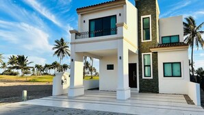A modern two-story house with a balcony, large windows, and a stone facade. - Hermosa casa vacacional (Mazatlán)