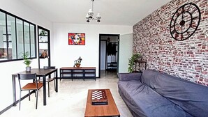 A modern living room with a brick wall, a gray sofa, a wooden coffee table, and a dining area with a table and chairs.