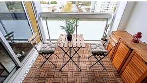 A balcony with a wooden floor, a table with chairs, a potted plant, a wooden cabinet, and a red lantern.