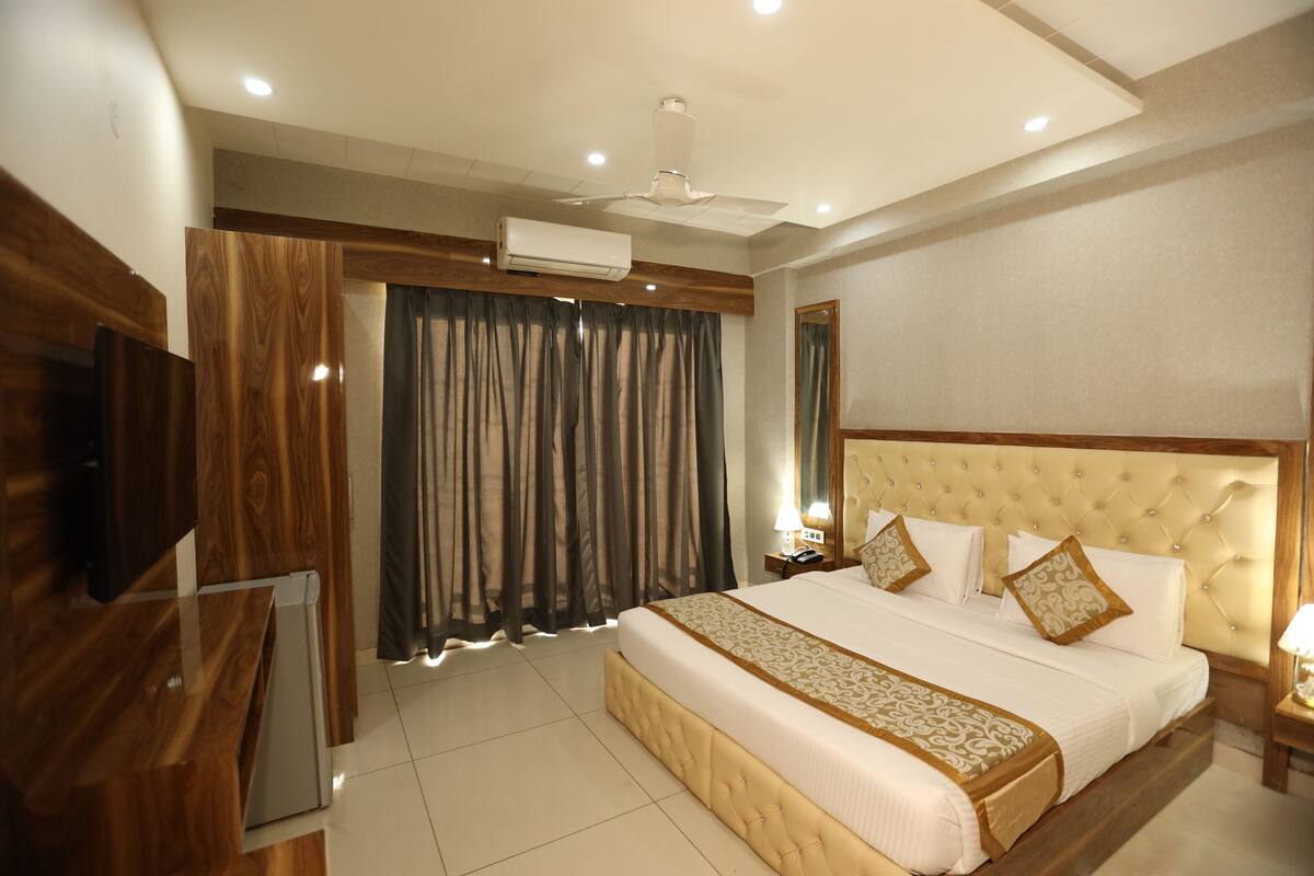 Een hotelkamer met een groot bed, een plafondventilator, een airconditioning, een televisie en een nachtkastje met een lamp.