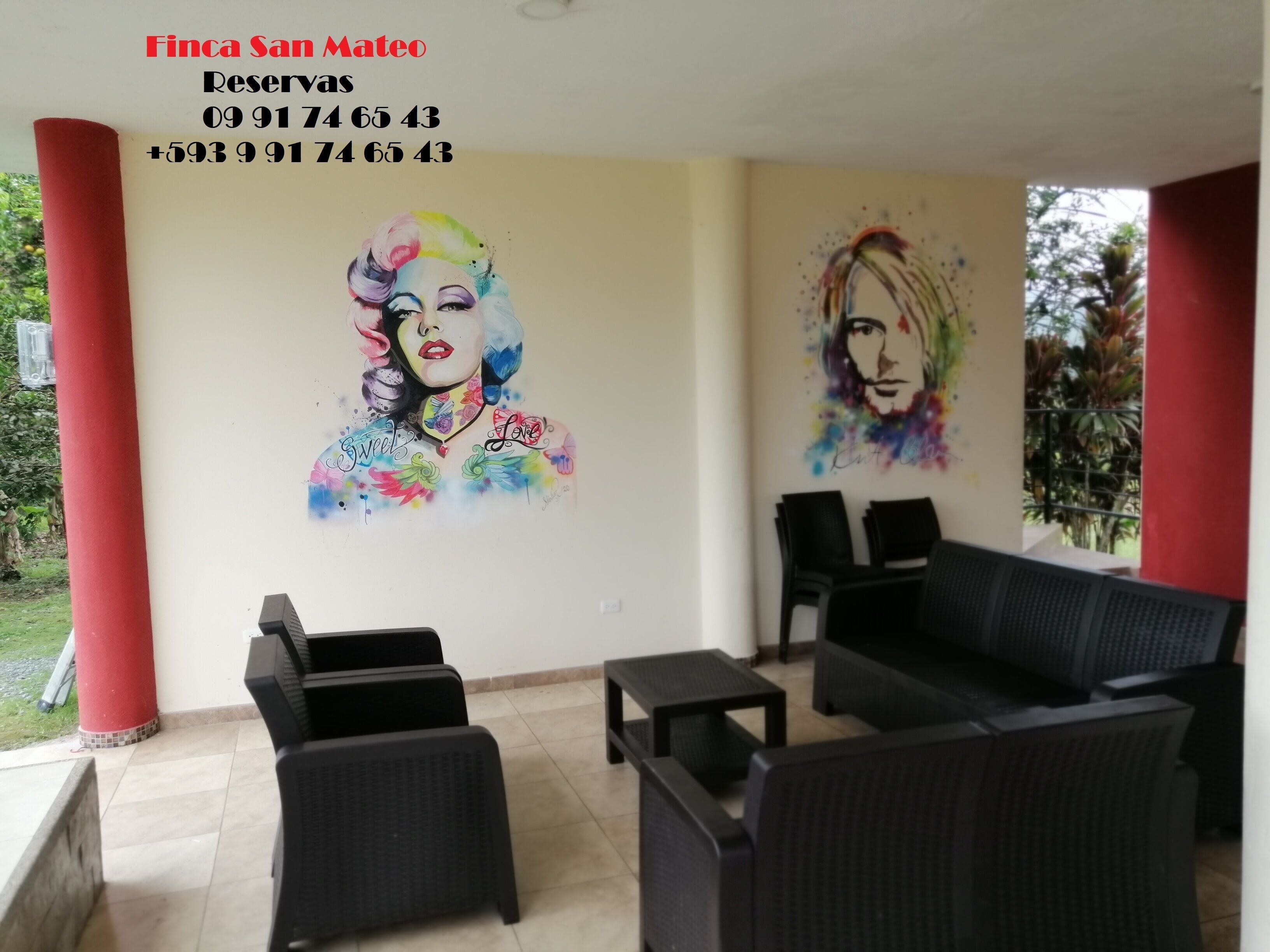A room with two black sofas, a small table, and a red pillar. There are two colorful wall art pieces depicting women with floral designs and the words "Sweet's Love".