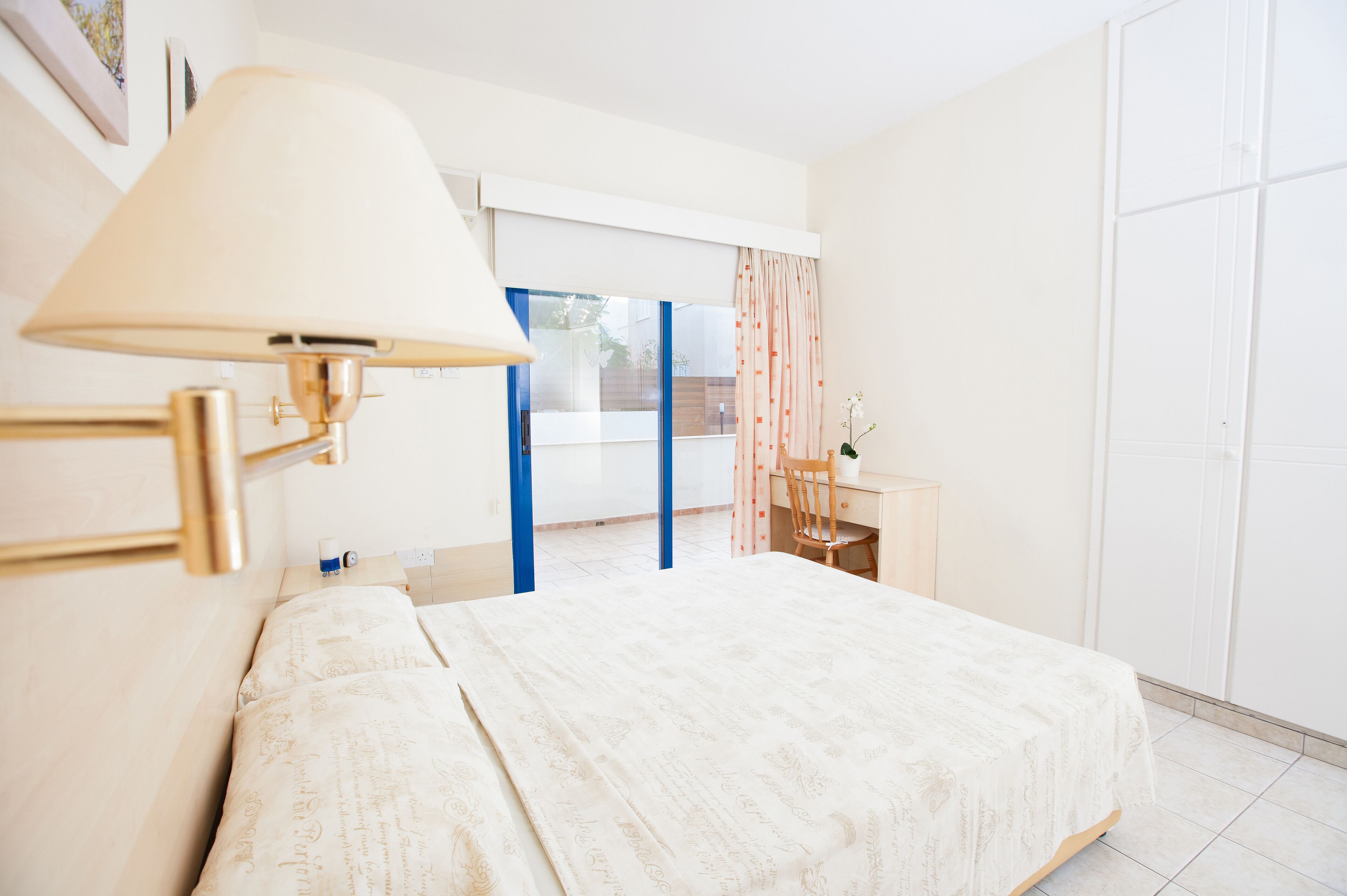Un dormitorio con cama, mesita de noche, lámpara, silla y ventana con cortinas.