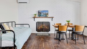 A room with a bed, a fireplace, a dining table with chairs, and a white brick wall. - Alps Lakeview Lodge (East Jindabyne)