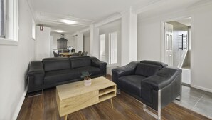 A modern living room with a black leather sofa, a wooden coffee table, and a black armchair. A kitchen area is visible in the background. - Alps Lakeview Lodge (East Jindabyne)