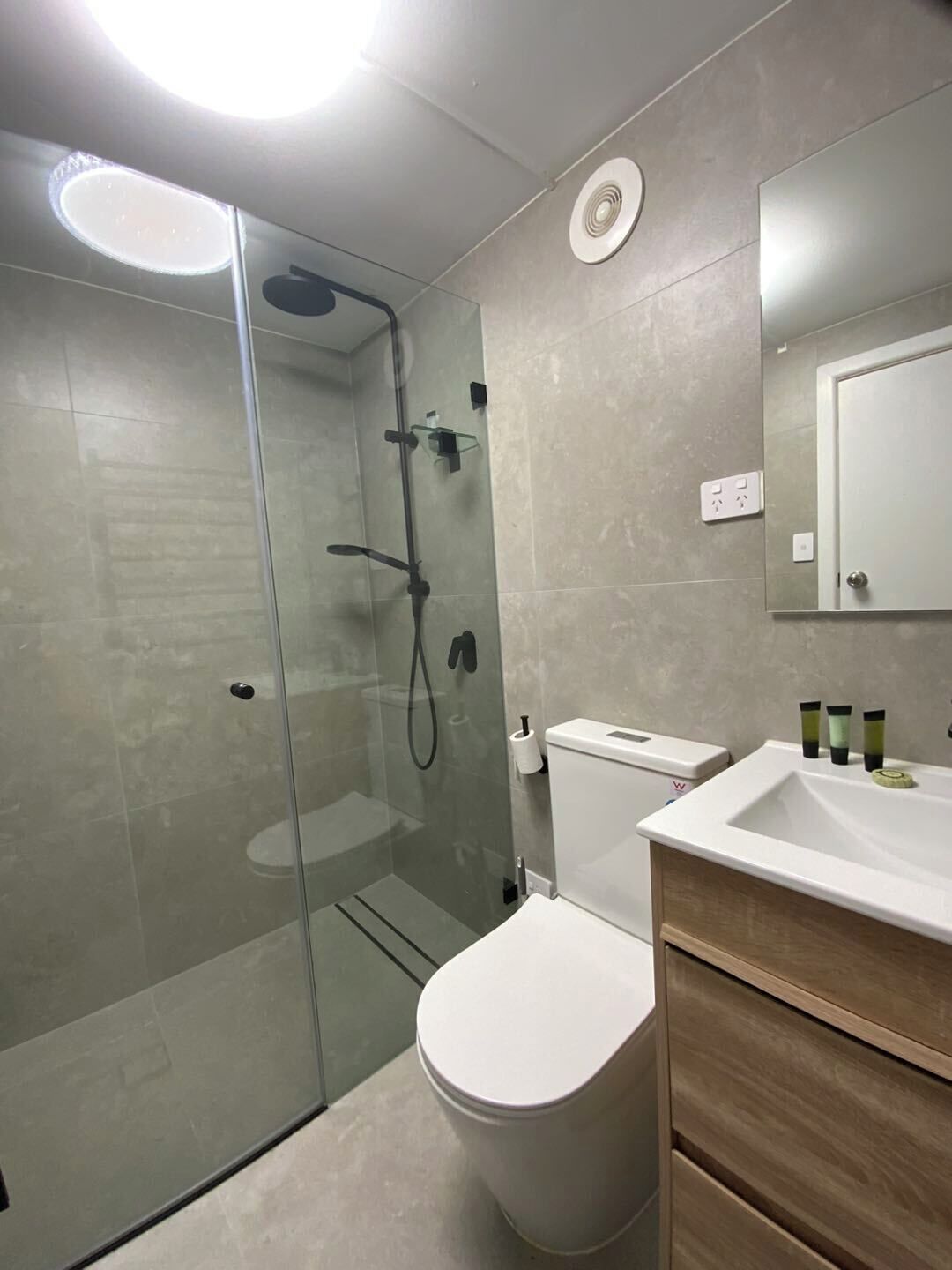 Une salle de bain moderne avec une douche à parois de verre, des toilettes blanches et un meuble-lavabo en bois avec un évier.