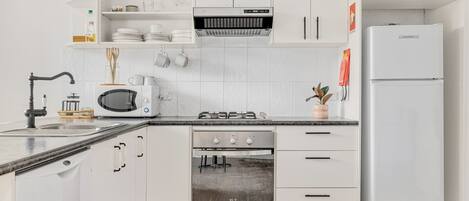Una cocina moderna con armarios blancos, un microondas integrado, una estufa a gas y un refrigerador blanco.